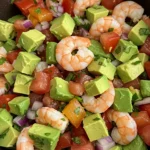 Shrimp ceviche salad with avocado chunks, tomatoes, onions, and cilantro in a dark brown bowl, close-up