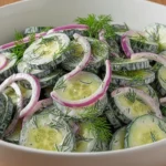 Cucumber onion salad with creamy dressing and dill in a large white bowl on a wooden surface