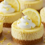 Mini lemon cheesecakes with whipped cream and lemon slices, served on parchment over a rustic wooden board