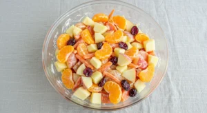 Top-down view of a glass bowl filled with vibrant carrot apple salad featuring mandarin oranges and cranberries on a striped placemat