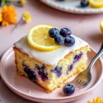 Top view of lemon blueberry sheet cake on a pink plate, decorated with lemon slice, glaze, and fresh blueberries in soft lighting.