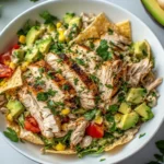 Overhead view of a Santa Fe chicken salad in a white bowl with avocado, corn, tomatoes, tortilla strips, and creamy dressing