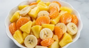 Bowl of sunshine salad with pineapple, bananas, and mandarin oranges coated in a creamy vanilla sauce on a marble countertop.
