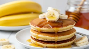 Fluffy Brown Sugar Banana Pancakes stacked on a plate with maple syrup
