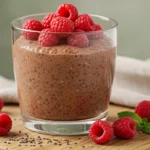 Glass cup of creamy chocolate chia pudding topped with raspberries on rustic wooden board with natural light