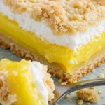 Zoomed-in photo of lemon cream cheese dump cake showing yellow filling, golden-brown crust, and off-white meringue on patterned plate
