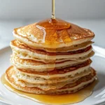 Stack of light beige oatmeal pancakes with golden edges, drizzled with warm honey on a white plate
