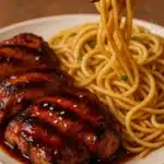 Grilled teriyaki chicken with garlic noodles, garnished with sesame seeds and green onions.