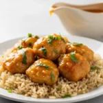 Plate of honey garlic chicken glazed with light orange sauce, garnished with fresh herbs, over brown rice on a gray countertop