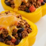 Close-up of taco stuffed yellow bell pepper filled with seasoned beef, black beans, diced tomatoes, and melted cheese on a white plate
