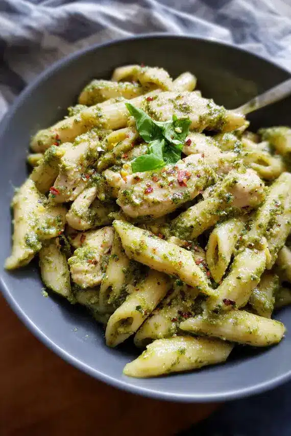 Freshly made pesto chicken pasta in a white bowl, showing vibrant green sauce coating spiral pasta and chunks of golden chicken