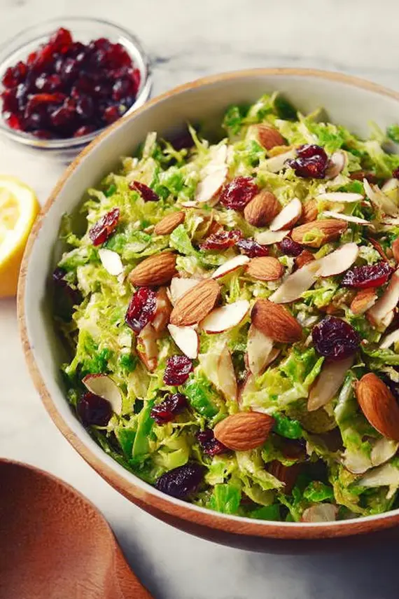 Freshly prepared shaved brussel sprout salad with toasted almonds and dried cranberries in a white bowl