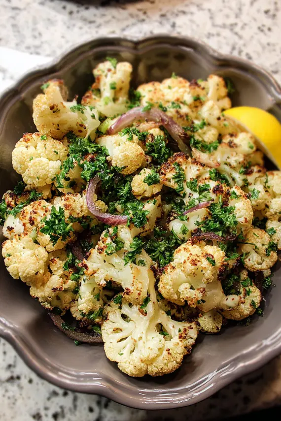 Roasted cauliflower salad with golden brown florets arranged on a serving platter with fresh herbs and lemon wedges