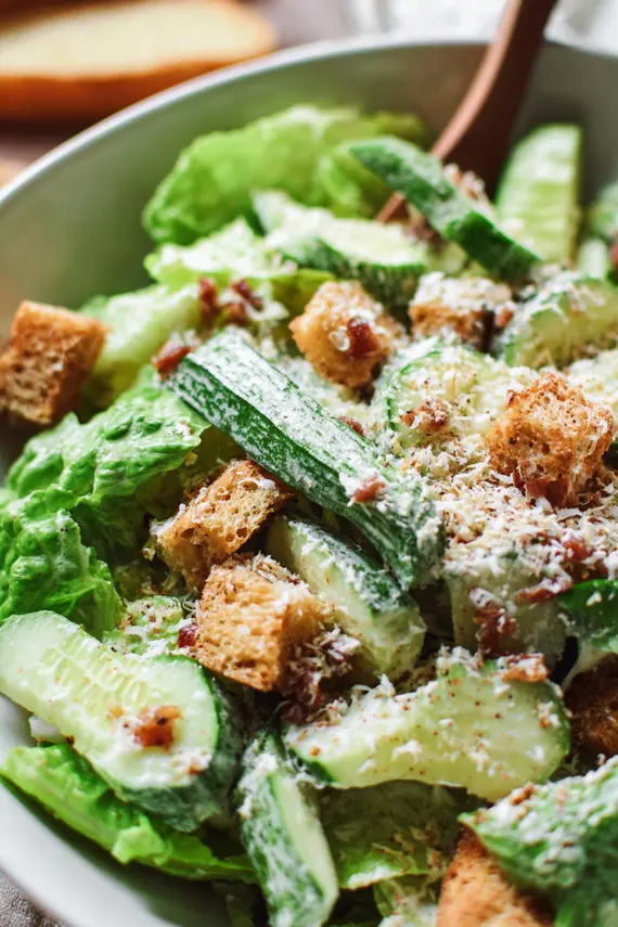 Fresh cucumber caesar salad in a large white bowl with Parmesan cheese and croutons on top