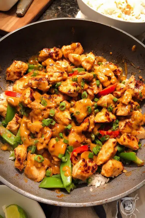 Easy peanut chicken recipe served over rice with garnishes of green onions and crushed peanuts