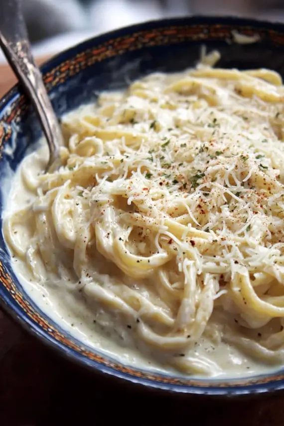 Homemade alfredo sauce being poured over fettuccine pasta