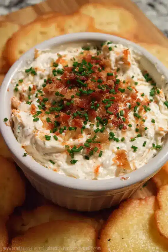 Herb cream cheese dip in a white bowl surrounded by fresh vegetables and crackers