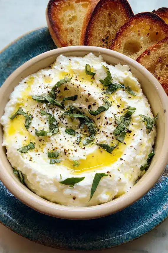 Herb ricotta dip served with colorful vegetables and crostini on a wooden board