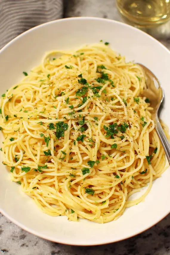 Close-up of mizithra cheese sauce being poured over freshly cooked spaghetti