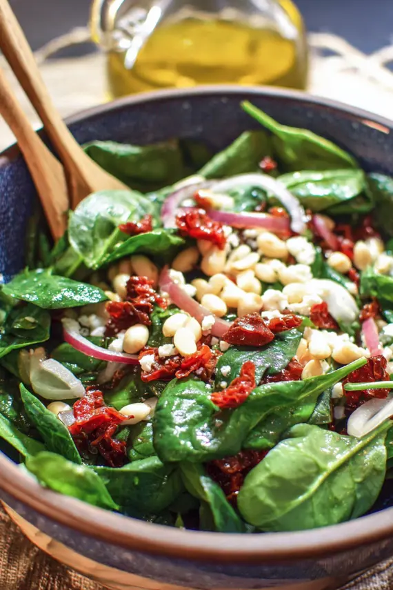 Sicilian spinach salad served in a beautiful bowl with pine nuts and sun-dried tomatoes