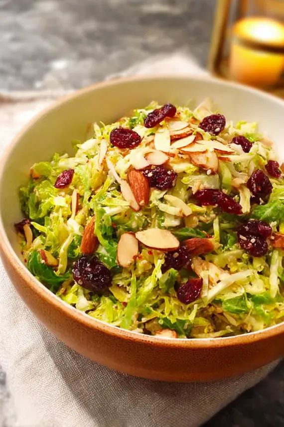 Shaved brussel sprout salad with almonds and cranberries served on a white plate as a side dish