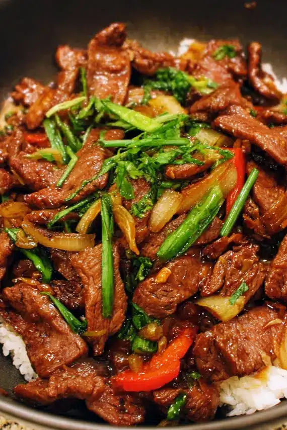 Close-up of glossy Asian stir fry sauce being poured over beef and vegetables