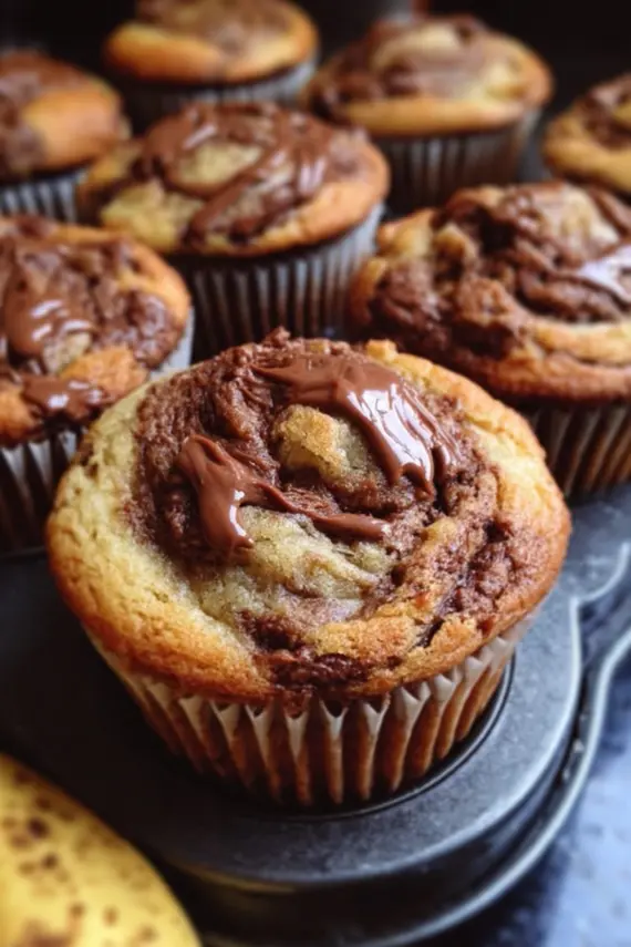 Freshly baked nutella swirled banana muffins with perfect golden tops and visible Nutella swirls