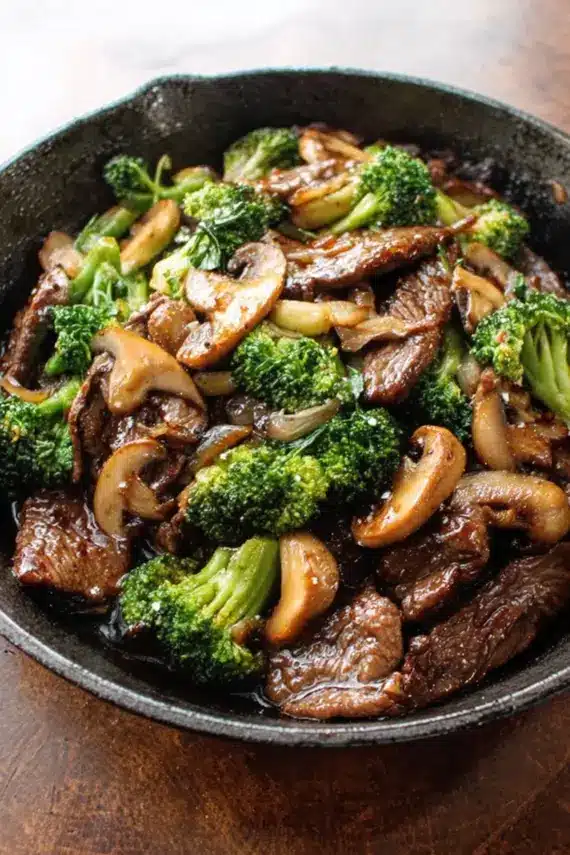 Beef broccoli mushroom stir fry in a wok with steam rising and vibrant colors
