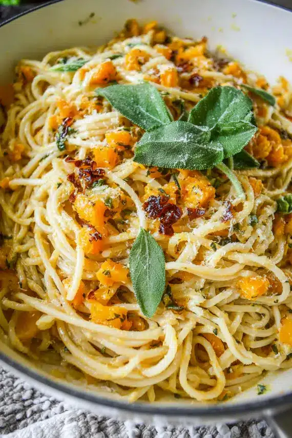 Close-up of butternut squash cubes being added to pasta in a pan