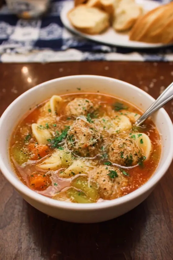 Close-up of perfectly formed parmesan meatballs in a rich, herb-flecked broth