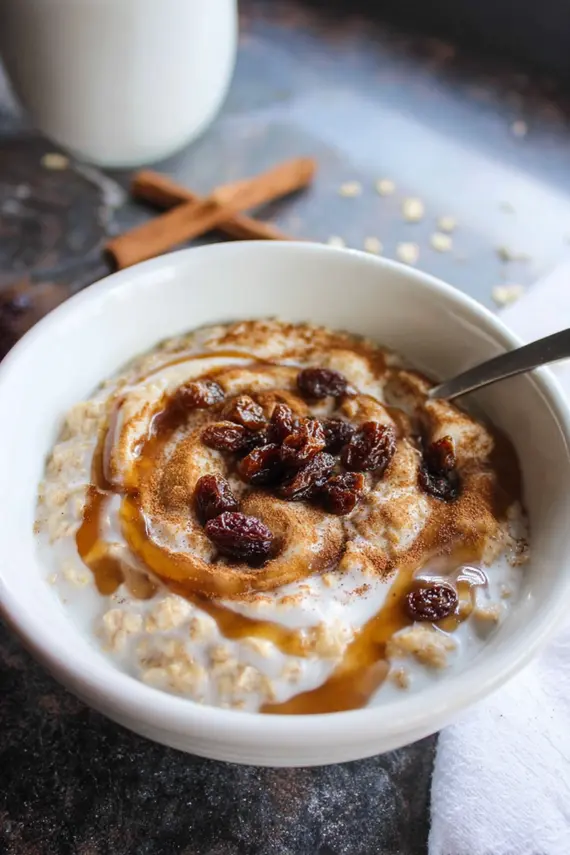 Creamy cinnamon roll oatmeal in a white bowl topped with yogurt swirl and nuts
