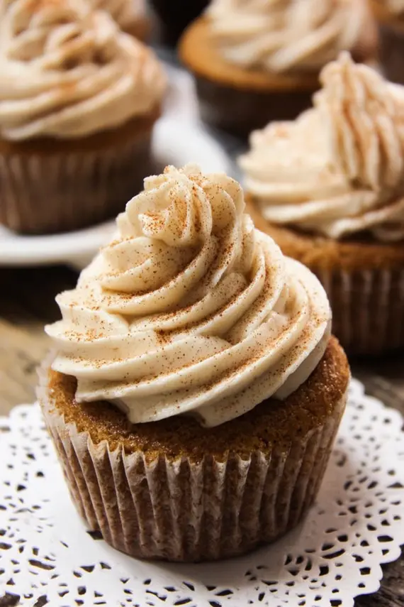 Close-up of creamy cinnamon cream cheese frosting being piped onto spice cake cupcakes