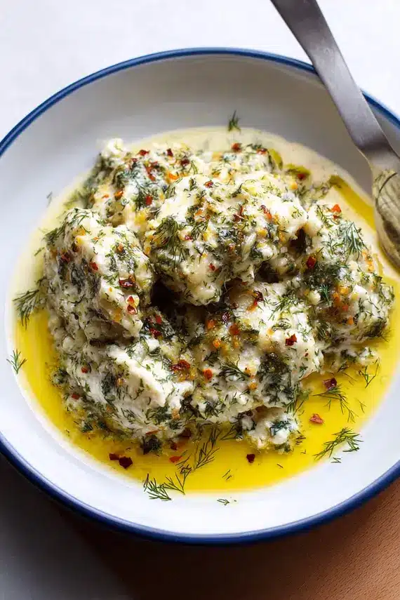 Homemade dill sauce being drizzled over Greek dumplings