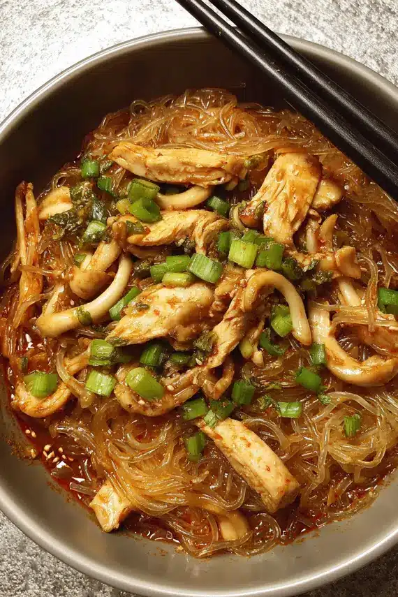 A bowl of gochujang chicken glass noodles garnished with green onions and sesame seeds