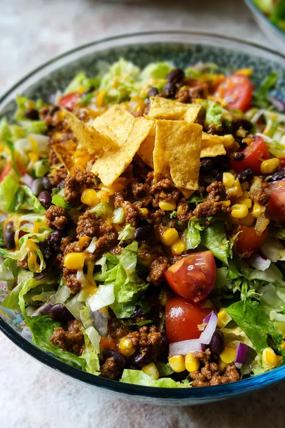 Ground beef taco salad ingredients arranged before mixing, showing colorful layers of meat, vegetables and toppings