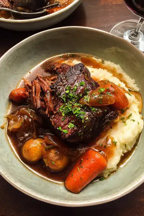 Close-up of herb jus being poured over braised beef chuck in a serving dish