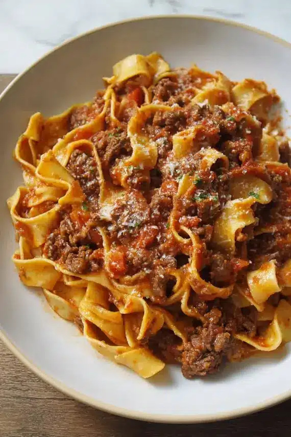 Homemade beef ragu sauce being served over freshly cooked pappardelle pasta