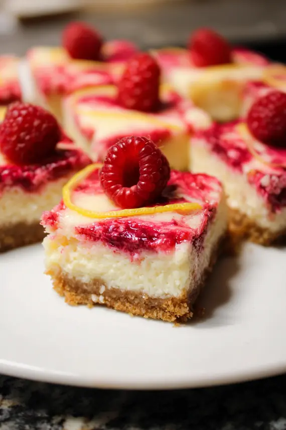 Sliced swirled raspberry lemon cheesecake bars arranged on a serving plate with fresh raspberries