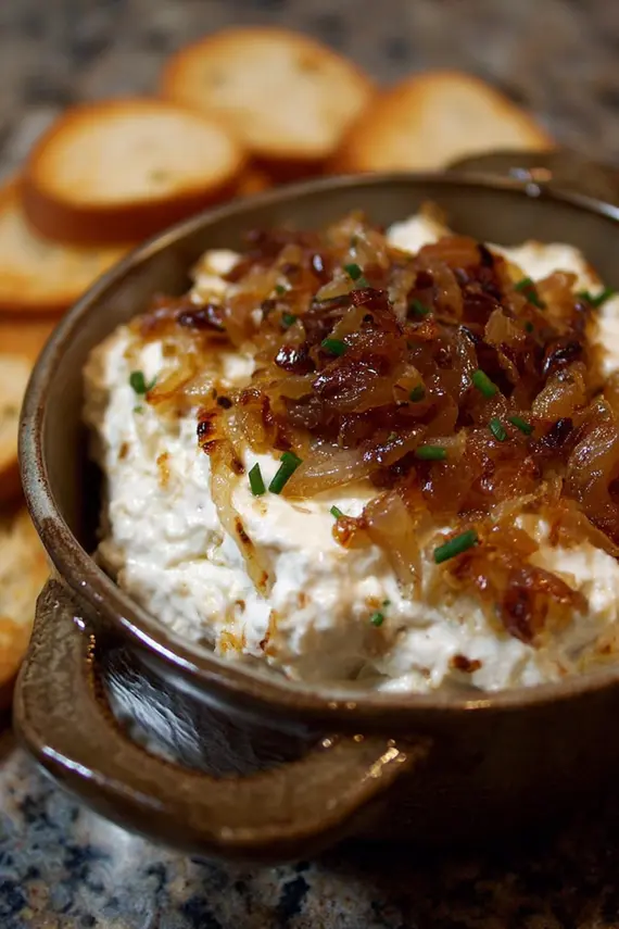 Creamy caramelized onion dip in a bowl with potato chips surrounding it