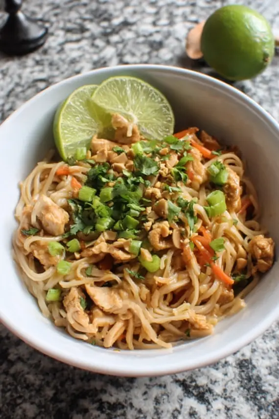 Close-up of Thai Peanut Chicken Noodles with garnishes and chopsticks