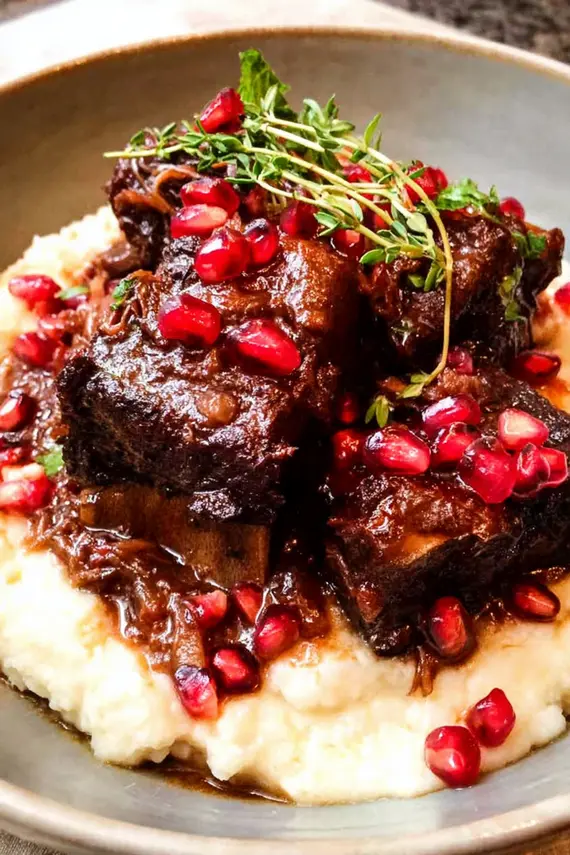 Close-up of glossy pomegranate demi glace being poured over braised short ribs