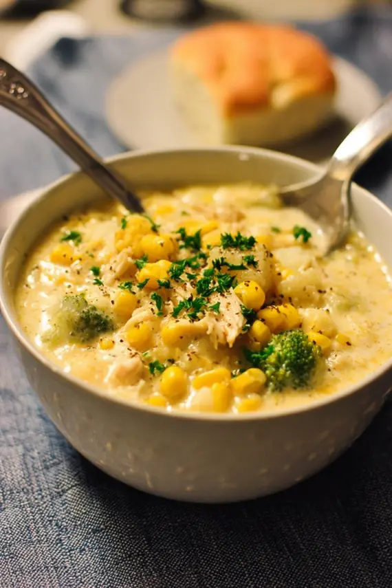 Chicken potato broccoli corn chowder served in a rustic bowl with bread on the side and garnished with fresh herbs