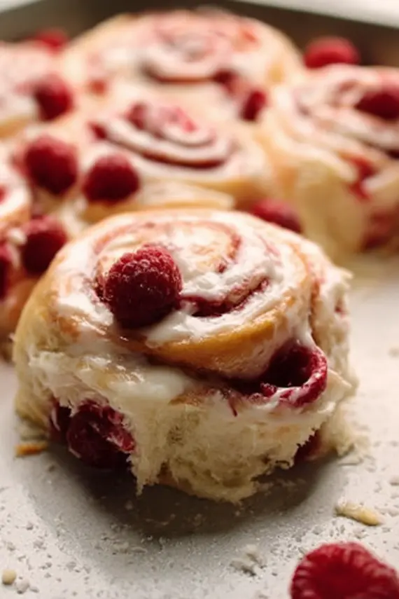 Freshly baked raspberry sweet rolls with glaze being poured over the top