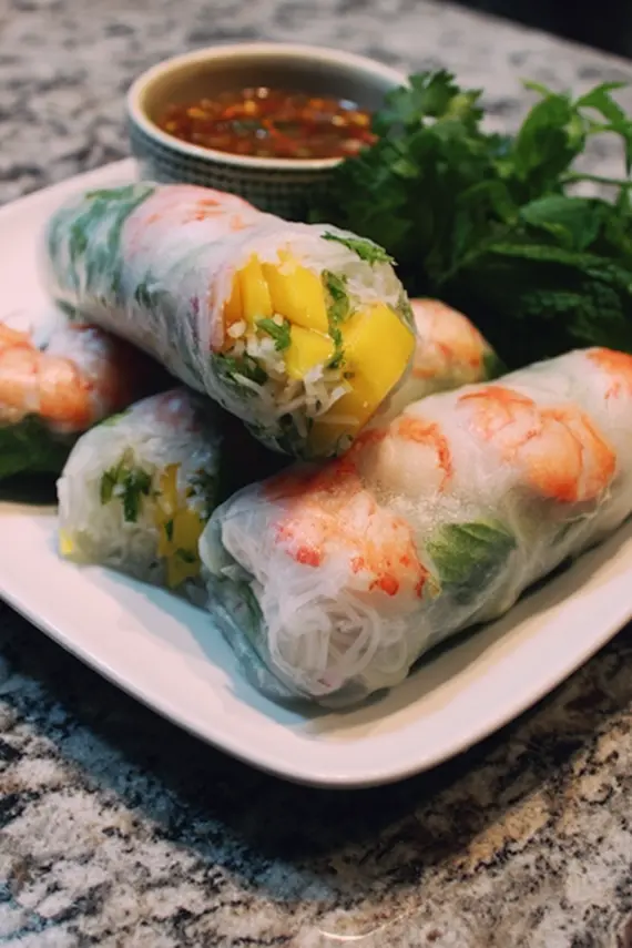Freshly made Shrimp Mango Rice Paper Rolls arranged on a white serving platter with dipping sauce in a small bowl