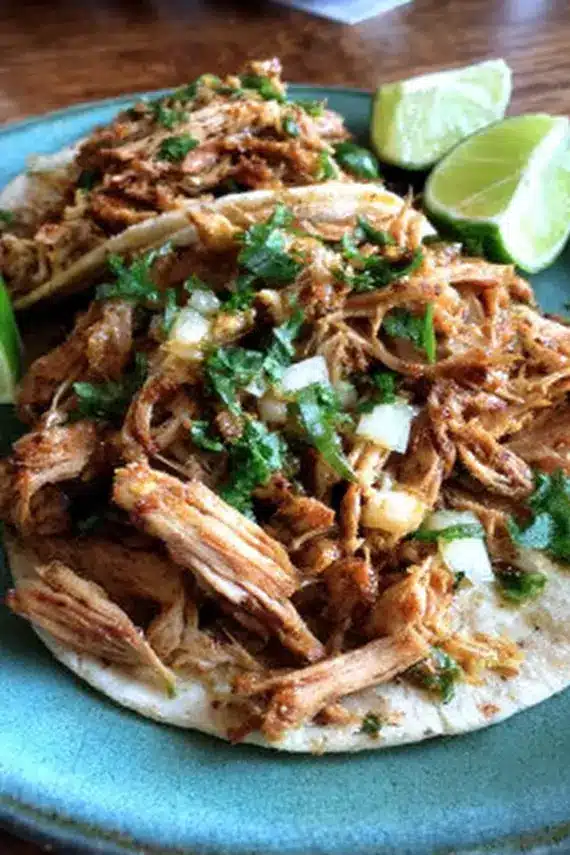 Perfectly cooked slow cooker chicken carnitas being shredded with two forks, showing the tender, juicy texture of the meat