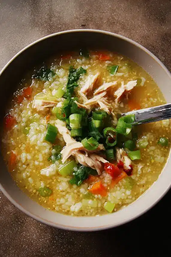 Steaming bowl of spicy ginger chicken rice soup with garnishes