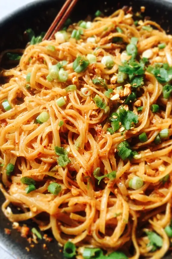 Sweet Spicy Garlic Noodles in a bowl garnished with green onions and sesame seeds