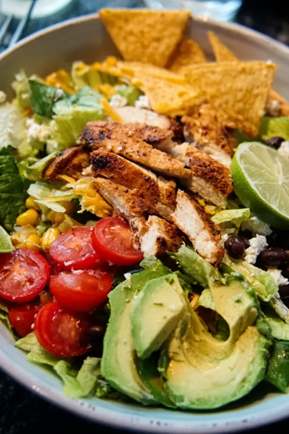 Homemade taco salad dressing being poured over a chicken taco salad