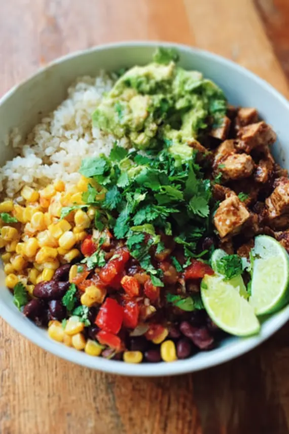 Plant based vegan burrito bowls with colorful vegetables and tofu arranged in a white ceramic bowl