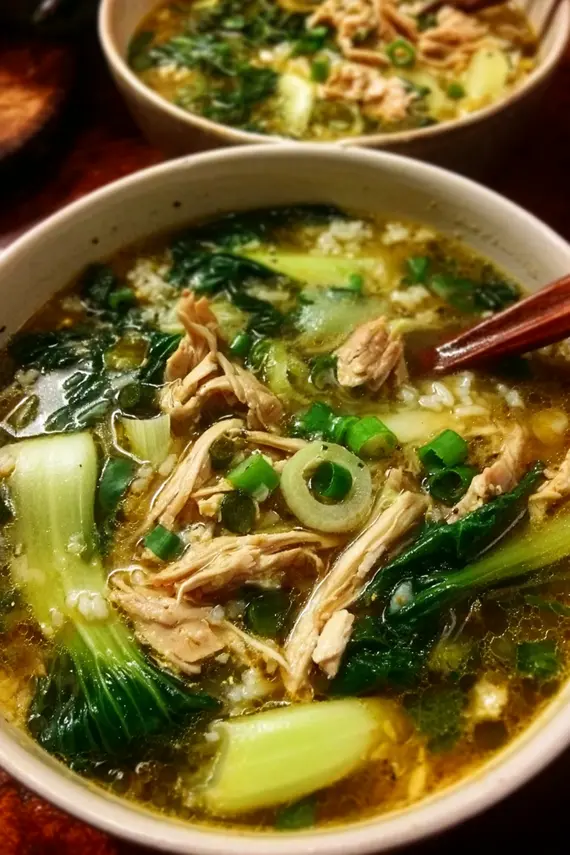 Fresh bok choy in a bowl next to prepared ginger chicken rice soup showing vibrant green leaves and tender stalks